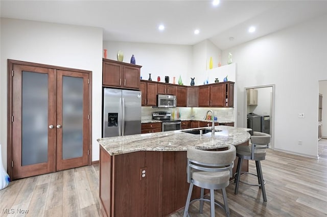 kitchen featuring stainless steel appliances, a sink, tasteful backsplash, light wood-style floors, and independent washer and dryer