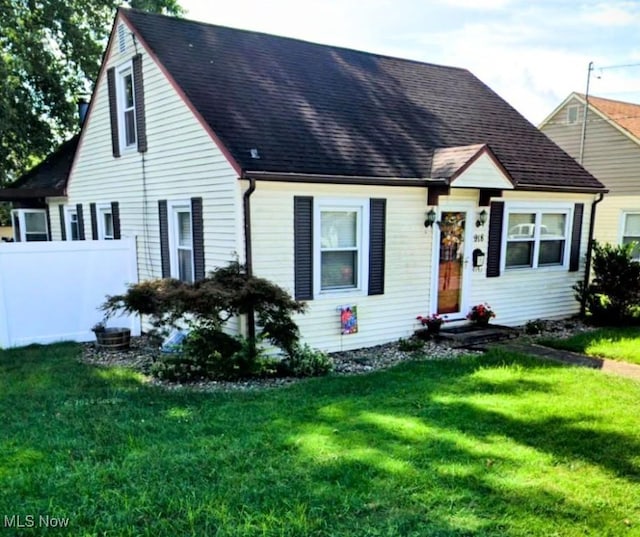 cape cod home with fence, roof with shingles, and a front yard