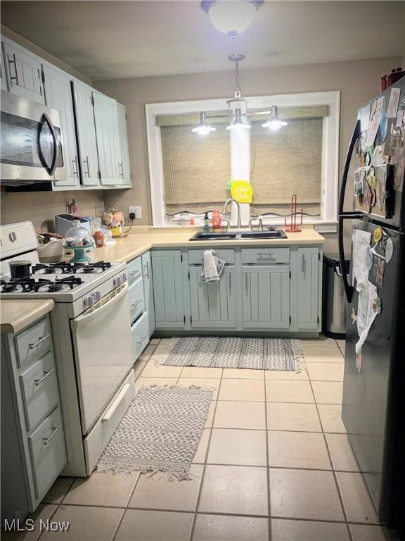 kitchen featuring a sink, white gas range oven, light countertops, stainless steel microwave, and freestanding refrigerator
