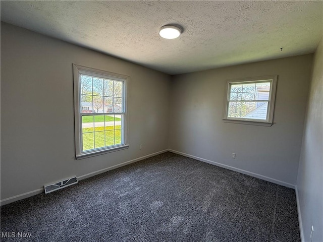 spare room with a textured ceiling, visible vents, dark carpet, and a healthy amount of sunlight
