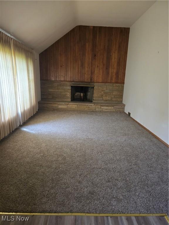 3742 Concord Dr, Beachwood, OH 44122 - unfurnished living room with lofted ceiling, a fireplace with raised hearth, wood walls, baseboards, and carpet flooring