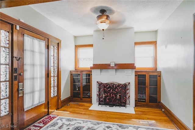 living room featuring wood finished floors, a brick fireplace, baseboards, and ceiling fan