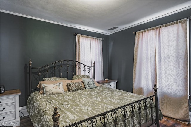bedroom with wood finished floors, visible vents, and ornamental molding