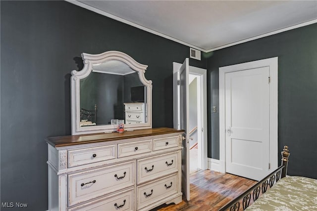 bedroom featuring baseboards, wood finished floors, visible vents, and crown molding