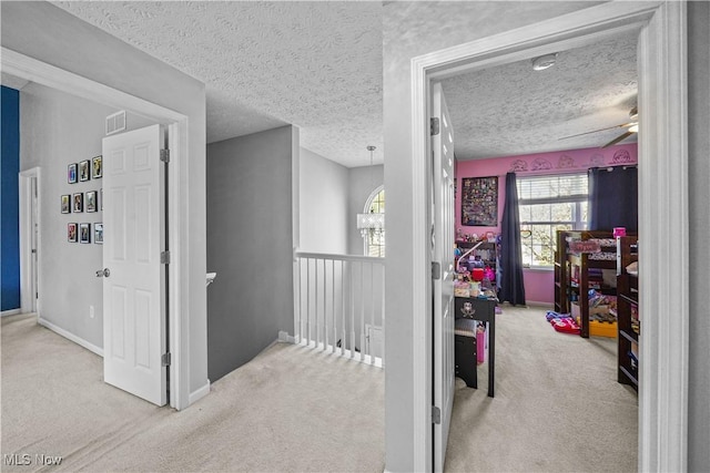 hall featuring visible vents, an upstairs landing, baseboards, a textured ceiling, and carpet flooring