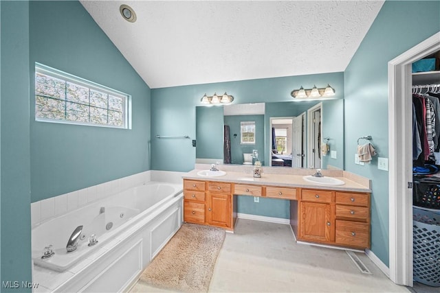 full bath with a textured ceiling, double vanity, a spacious closet, lofted ceiling, and a whirlpool tub
