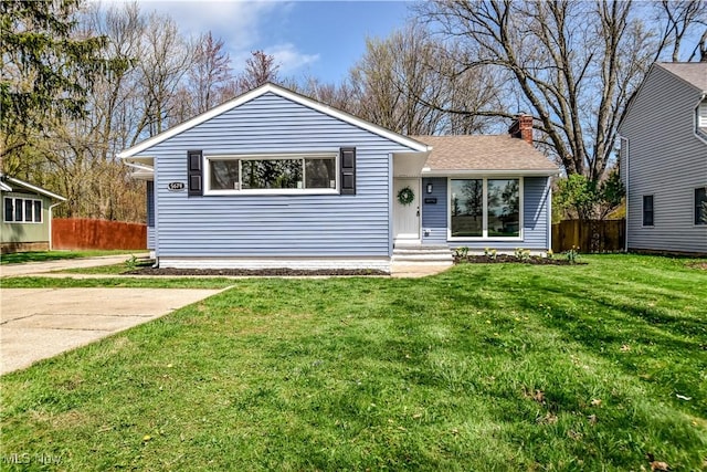 view of front of property with fence, a chimney, roof with shingles, and a front yard