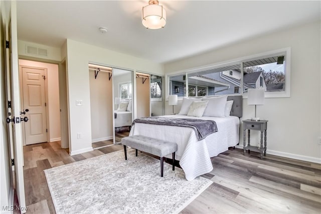 bedroom featuring two closets, visible vents, baseboards, and wood finished floors