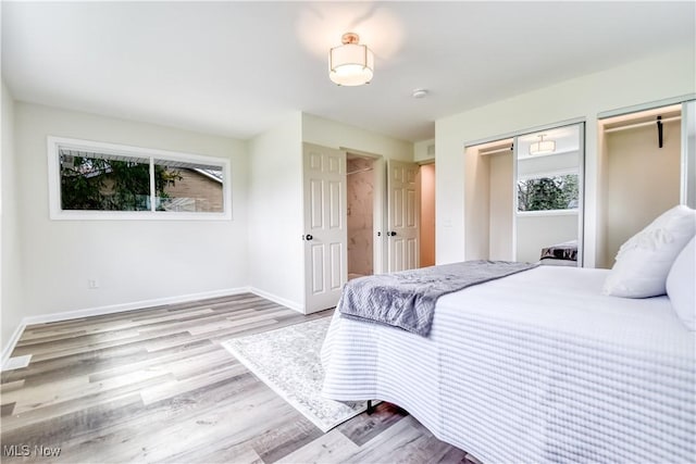 bedroom featuring multiple closets, baseboards, and wood finished floors