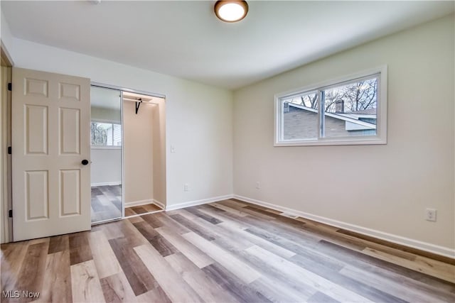 unfurnished bedroom featuring wood finished floors, a closet, and baseboards