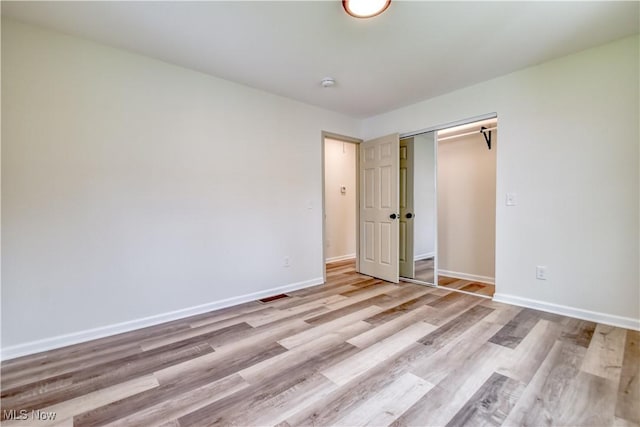 unfurnished bedroom featuring light wood-type flooring, baseboards, visible vents, and a closet