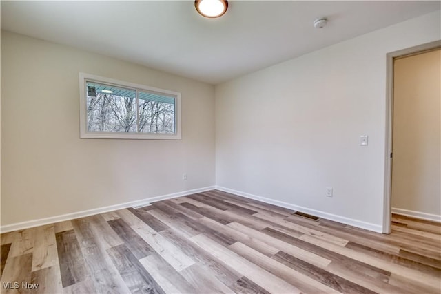 spare room with wood finished floors, visible vents, and baseboards