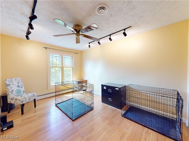 living area with track lighting, a ceiling fan, baseboards, light wood finished floors, and a textured ceiling
