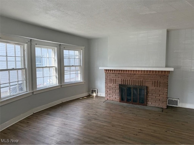 unfurnished living room with wood finished floors, visible vents, baseboards, a fireplace, and a textured ceiling