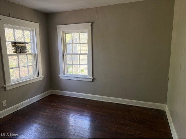 empty room with plenty of natural light, baseboards, and dark wood-type flooring