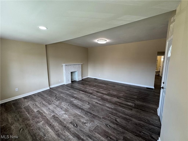 unfurnished living room featuring baseboards, recessed lighting, dark wood-style floors, and a brick fireplace