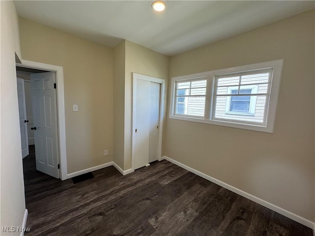 unfurnished bedroom with dark wood-style flooring, a closet, and baseboards