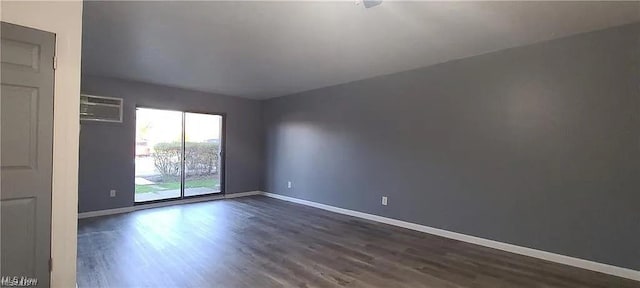spare room featuring a wall unit AC, baseboards, and dark wood-type flooring