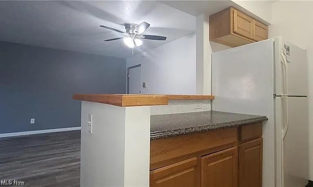 kitchen featuring dark stone countertops, freestanding refrigerator, ceiling fan, dark wood-style flooring, and baseboards