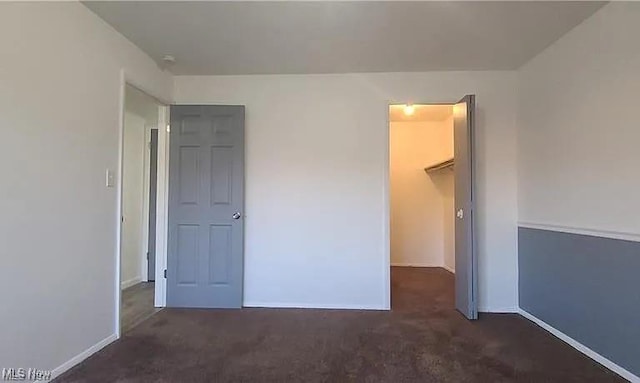 unfurnished bedroom featuring a spacious closet, carpet, and baseboards