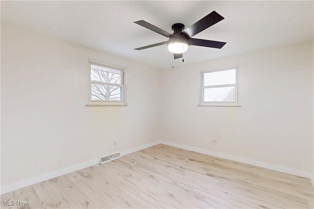 empty room with visible vents, a wealth of natural light, wood finished floors, and baseboards