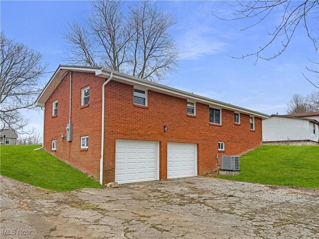 rear view of property featuring a garage, central AC unit, a yard, aphalt driveway, and brick siding