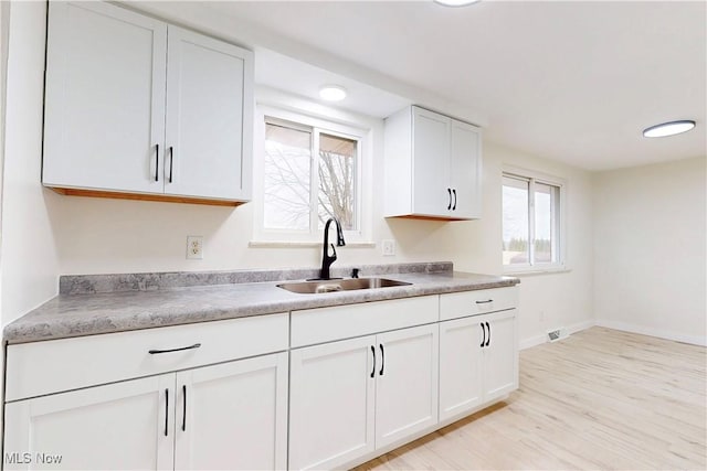 kitchen with a sink, light wood-type flooring, baseboards, white cabinetry, and light countertops