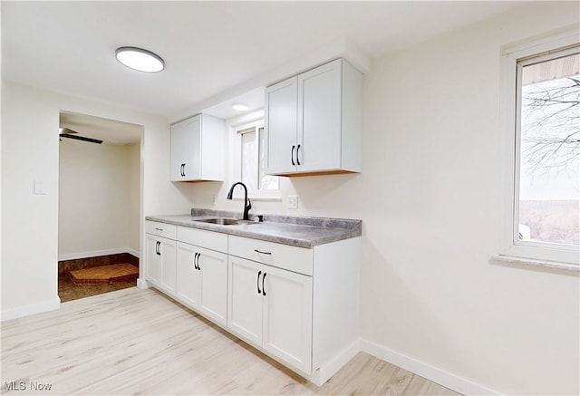 kitchen with baseboards, light wood-type flooring, white cabinets, and a sink
