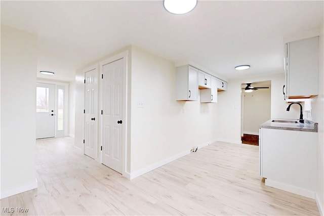 interior space with white cabinetry, a sink, baseboards, light wood-type flooring, and a ceiling fan