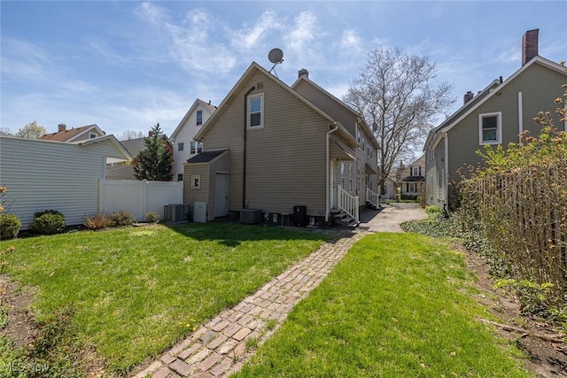 rear view of property featuring fence, a lawn, central air condition unit, and entry steps