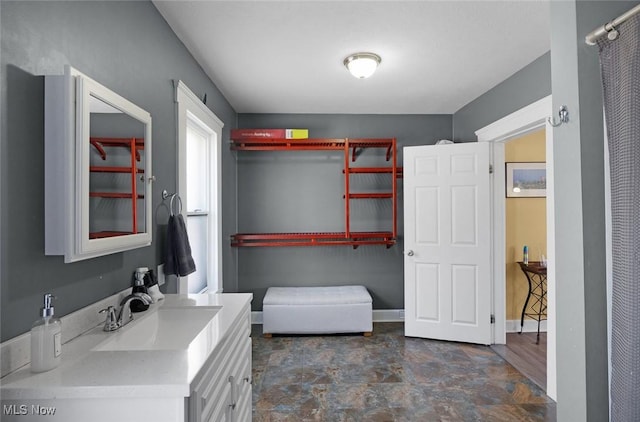 bathroom featuring stone finish floor, vanity, and baseboards