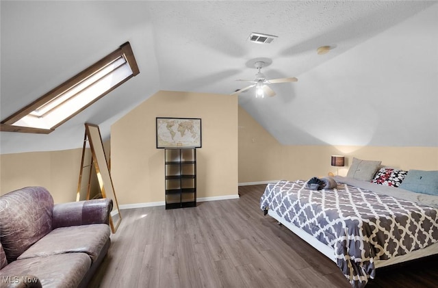 bedroom featuring vaulted ceiling with skylight, a ceiling fan, visible vents, baseboards, and wood finished floors