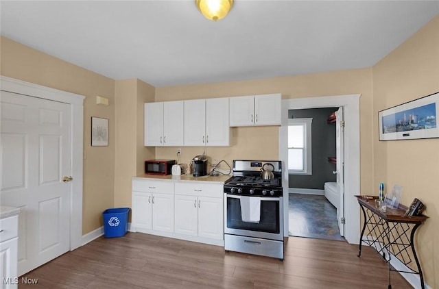 kitchen with stainless steel range with gas cooktop, black microwave, light countertops, white cabinets, and wood finished floors