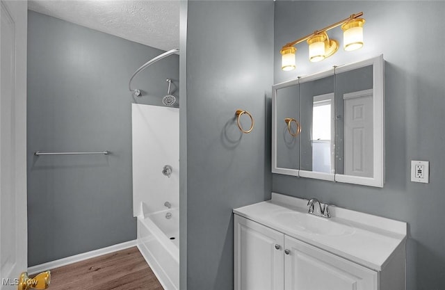 bathroom featuring a textured ceiling, tub / shower combination, baseboards, wood finished floors, and vanity