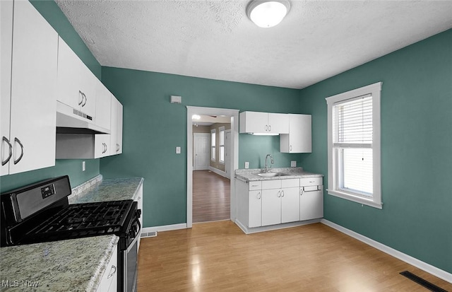 kitchen with under cabinet range hood, light countertops, gas stove, baseboards, and visible vents