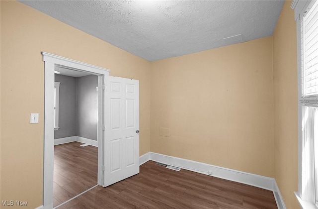 unfurnished bedroom featuring dark wood finished floors, baseboards, visible vents, and a textured ceiling