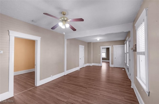 empty room featuring a wealth of natural light, wood finished floors, ceiling fan, and baseboards