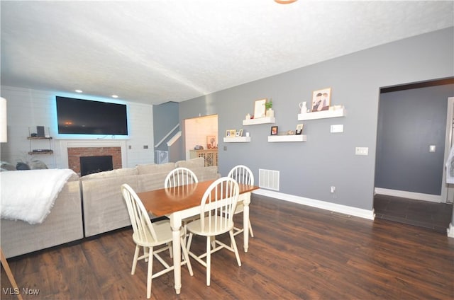 dining room with a fireplace, wood finished floors, visible vents, and baseboards