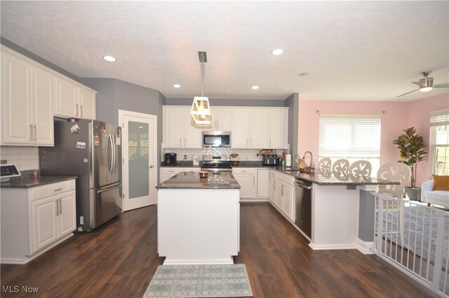 kitchen featuring decorative backsplash, stainless steel appliances, white cabinets, a sink, and a peninsula