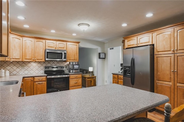 kitchen featuring recessed lighting, decorative backsplash, appliances with stainless steel finishes, a sink, and a peninsula