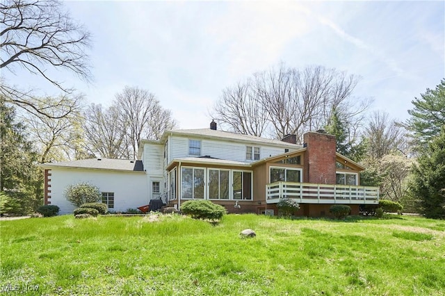 back of property featuring a lawn, a chimney, a wooden deck, and a sunroom