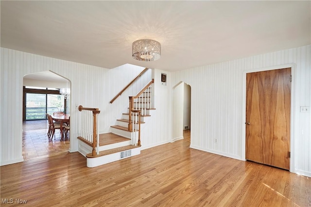 stairway featuring visible vents, arched walkways, an inviting chandelier, and wood finished floors