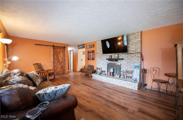living room with a textured ceiling, a barn door, wood finished floors, and a brick fireplace