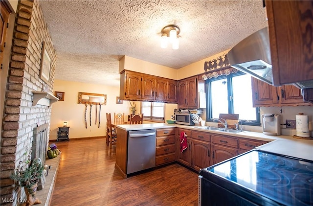 kitchen featuring a textured ceiling, a sink, appliances with stainless steel finishes, dark wood-type flooring, and a peninsula