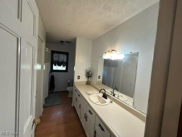 bathroom with toilet, a textured ceiling, wood finished floors, and vanity