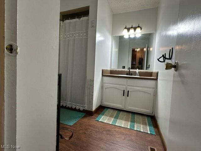 full bath with a shower with curtain, vanity, baseboards, a textured ceiling, and wood finished floors