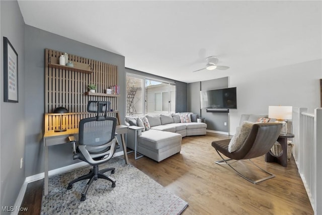 living area featuring wood finished floors, a ceiling fan, and baseboards