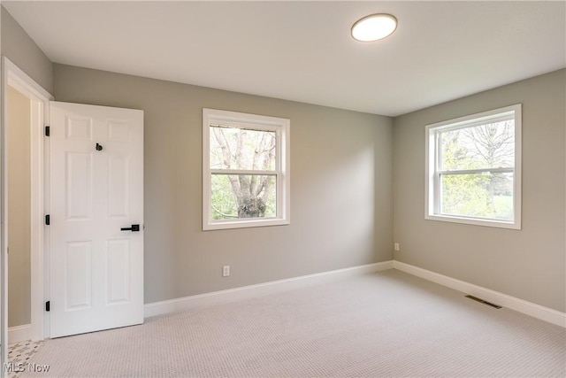 unfurnished room with visible vents, light colored carpet, and a healthy amount of sunlight