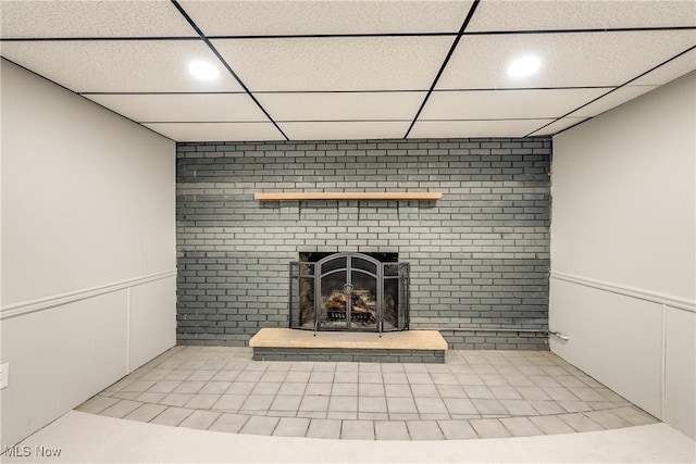 unfurnished living room with a brick fireplace, recessed lighting, a paneled ceiling, and wainscoting