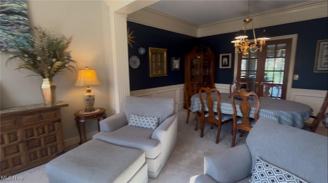carpeted dining area with a chandelier, wainscoting, crown molding, and a decorative wall